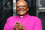 A photo of Desmond Tutu wearing purple clerical robes and spectacles, smiling