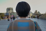 A woman with a short black bob haircut with her back to the camera with a university campus in the background.