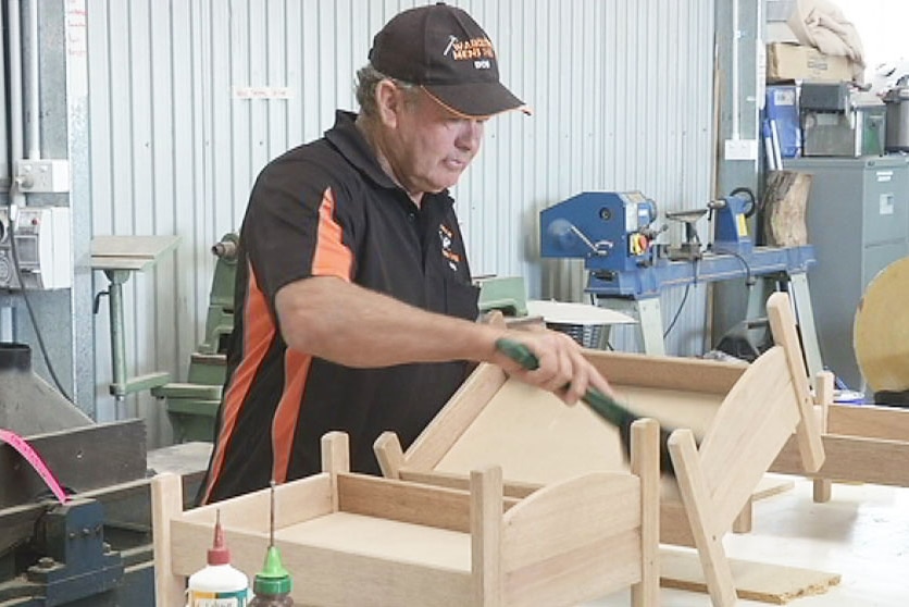 An older fellow busies himself with some woodwork in a tool shed.