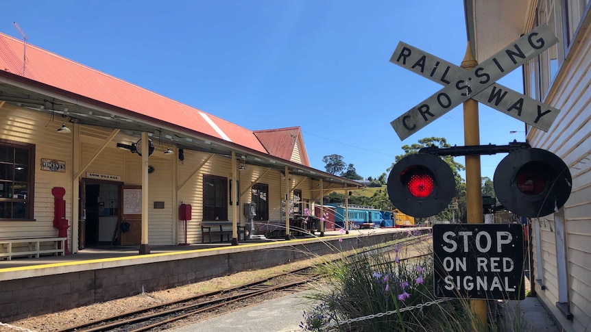 A weatherboard train station and railway crossing sign on a sunny day