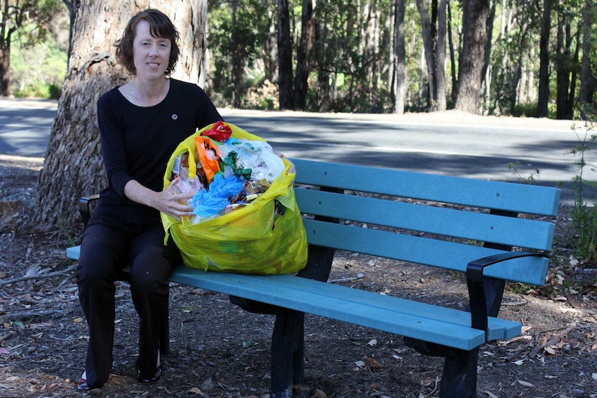 A woman sits on a bench holding a bag of plastic rubbish.