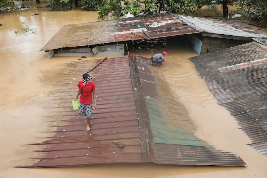 A man walks on top of a roof of a submerged house as floods inundate villages