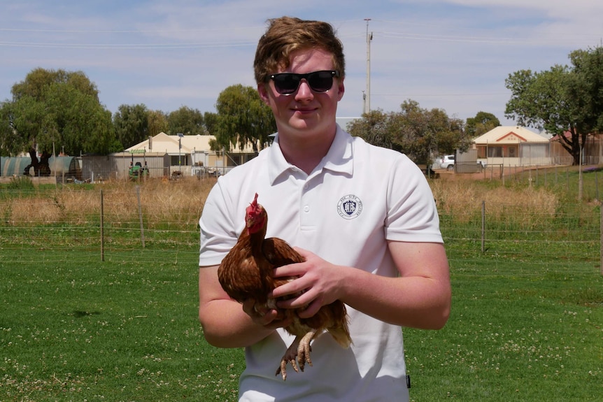 Year 12 student Adam McInnes holding a chicken and standing in the school agriculture plot