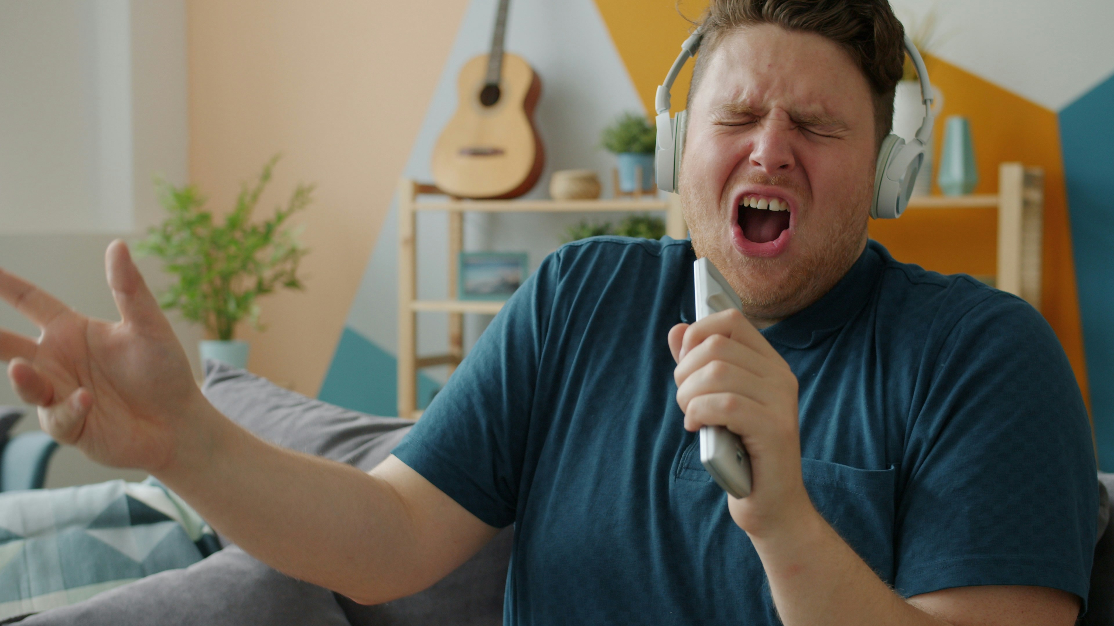 A young man screws his eyes shut while singing and gesturing into a remote control