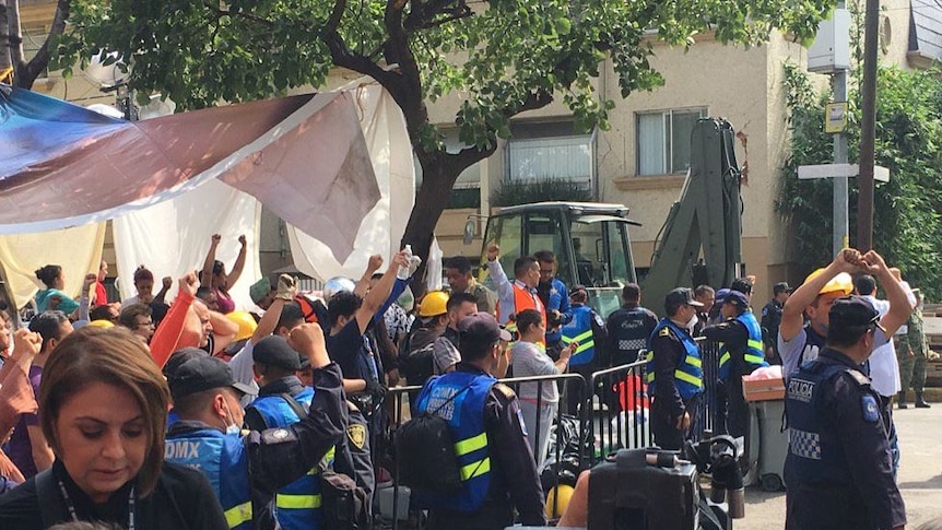 Rescue workers at the site of a collapsed school in Mexico City raise their arms to call for silence