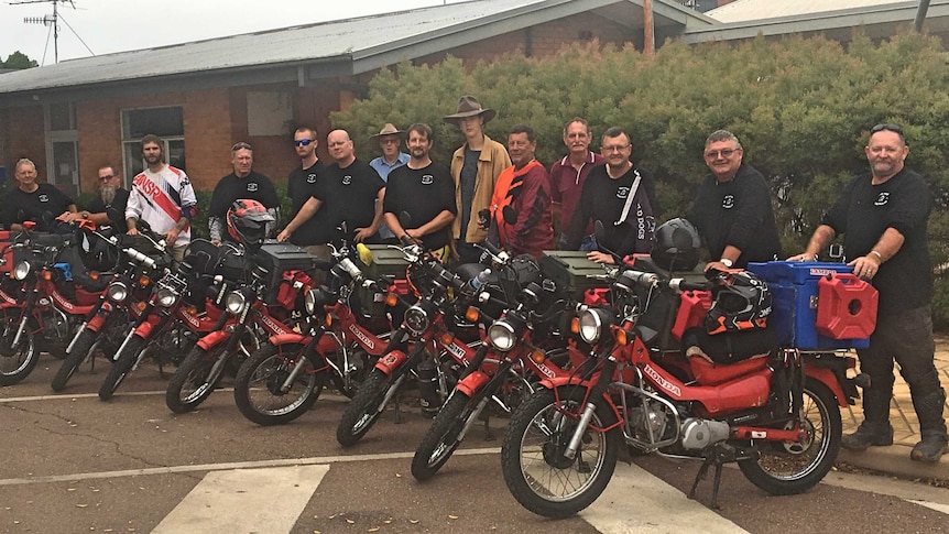 A line of red and black motorbikes parked on the side of a street with a group of men standing behind them.