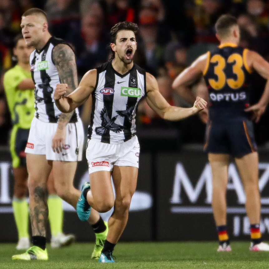 An AFL player runs away from goal with arms outstretched and fists clenched in celebration after a goal.