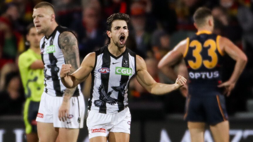 An AFL player runs away from goal with arms outstretched and fists clenched in celebration after a goal.