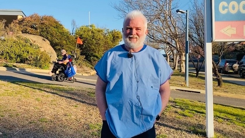 a man stands in scrubs smiling at the camera