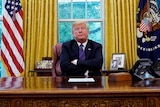 Donald Trump sits with his arms crossed at his desk