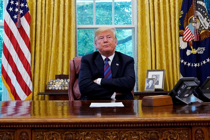 Donald Trump sits with his arms crossed at his desk