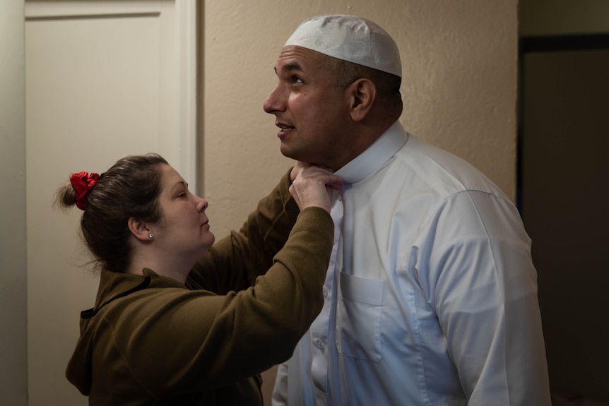 A woman buttons a man's collar.