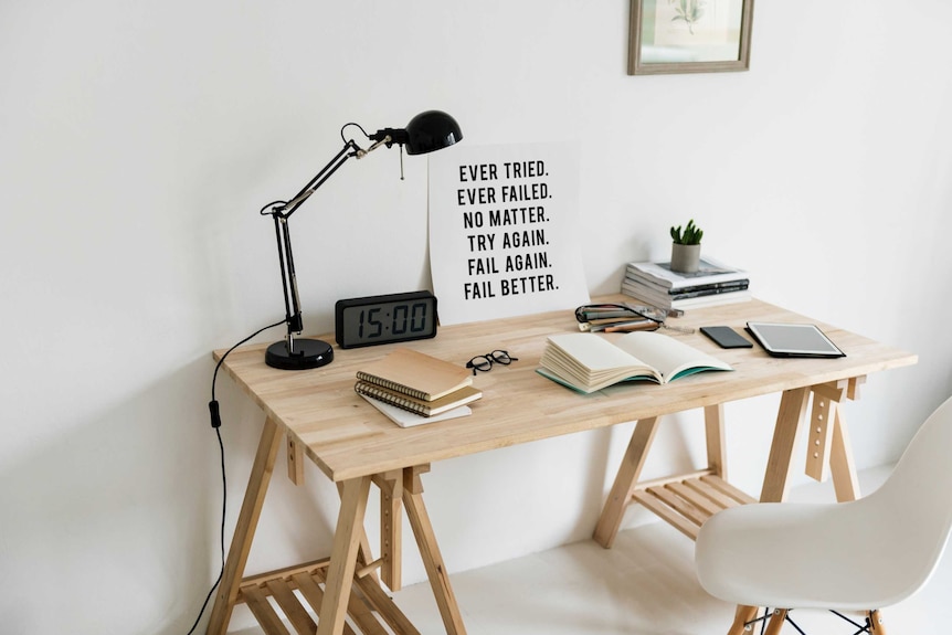 Desk with a poster saying 'ever tried, ever failed, no matter, try again, fail again' depicting the stress of imposter syndrome.