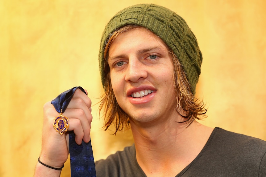 Nat Fyfe holds up the 2015 Brownlow Medal as he wears a green beanie and a grey shirt.