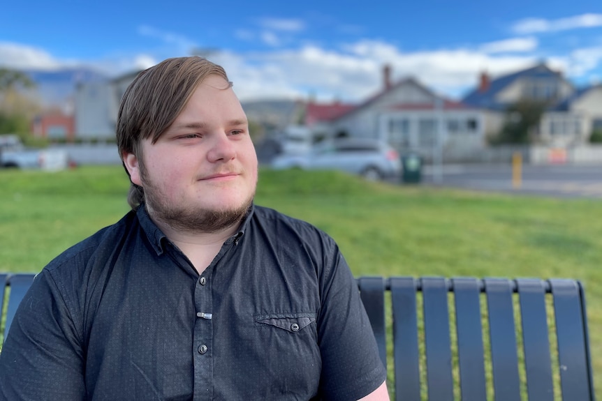 A young man wearing a navy blue shirt sits on a park bench.