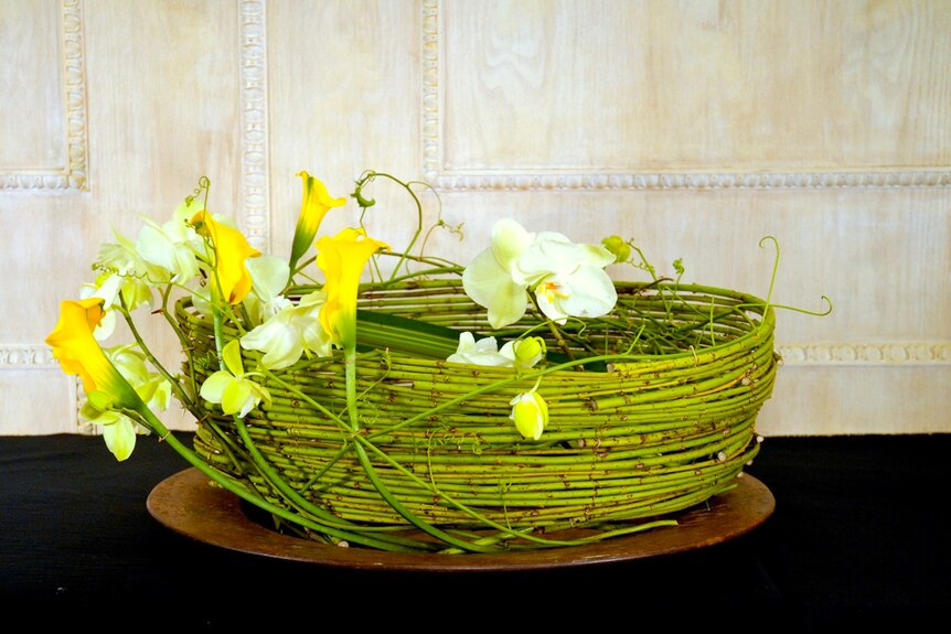 Yellow and white flowers sit upon a green basket made of bamboo.