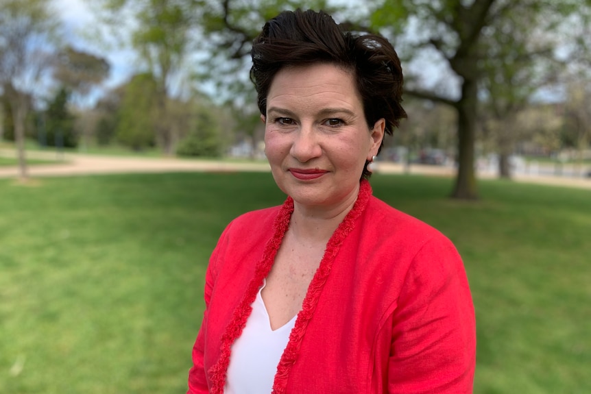 a woman in a red suit smiling in a park