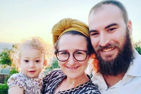 A young family poses together in front of light sunset.