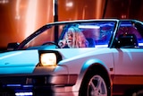 A man sings while sitting in a car with the headlights on, on stage during rehearsals for the Eurovision Song Contest.