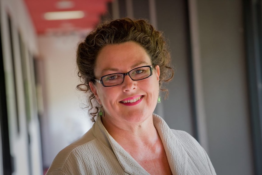 Catherine Bennett wears her hair tied up and glasses as she smiles at the camera.