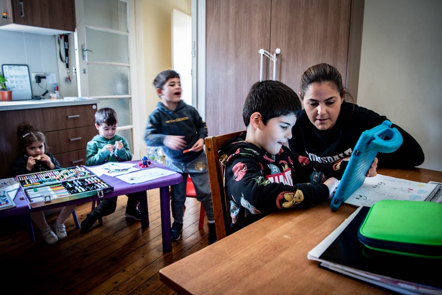 Mel Habib helps her 6-year-old son with school work while her three other kids colour in at a table in the kitchen. 