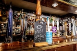 Beer taps with a sign reading 'miss you guys' next to a bottle of hand sanitizer