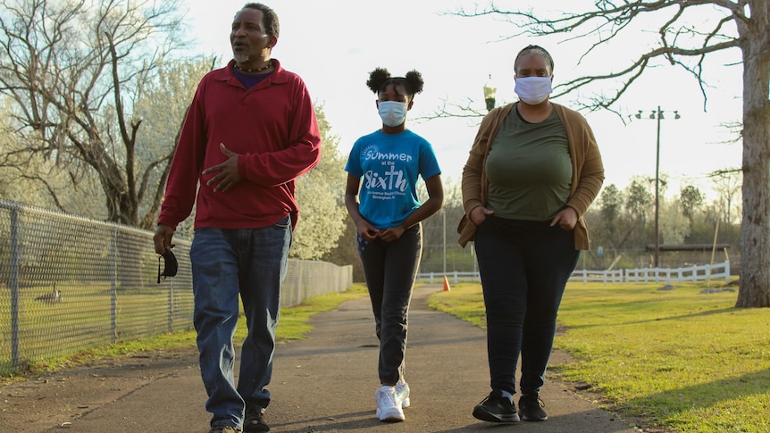 A man, woman and child walk along a path in a park at sunset