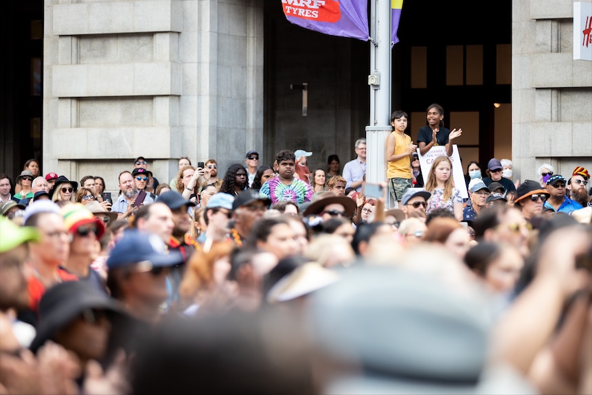 Two kids stand on top of a sea of people.