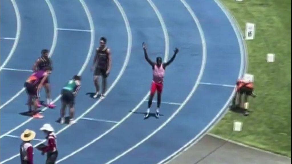A boy raises his hands on his head on an athletic track. Competitors are on their haunches around him.