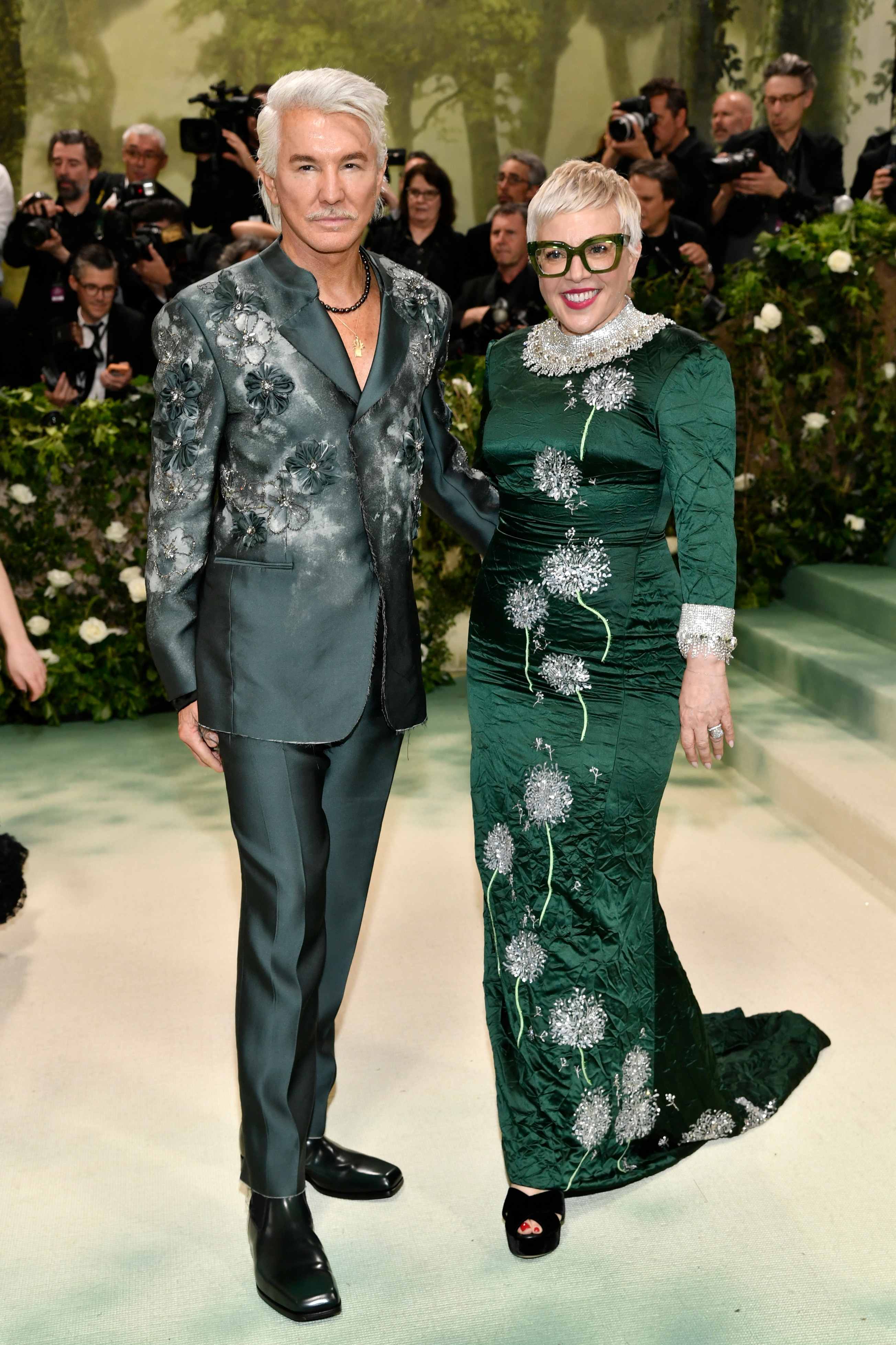 Baz Luhrmann wearing a dark green and silver suit and Catherine Martin in a dark green long sleeve dress with silver flowers