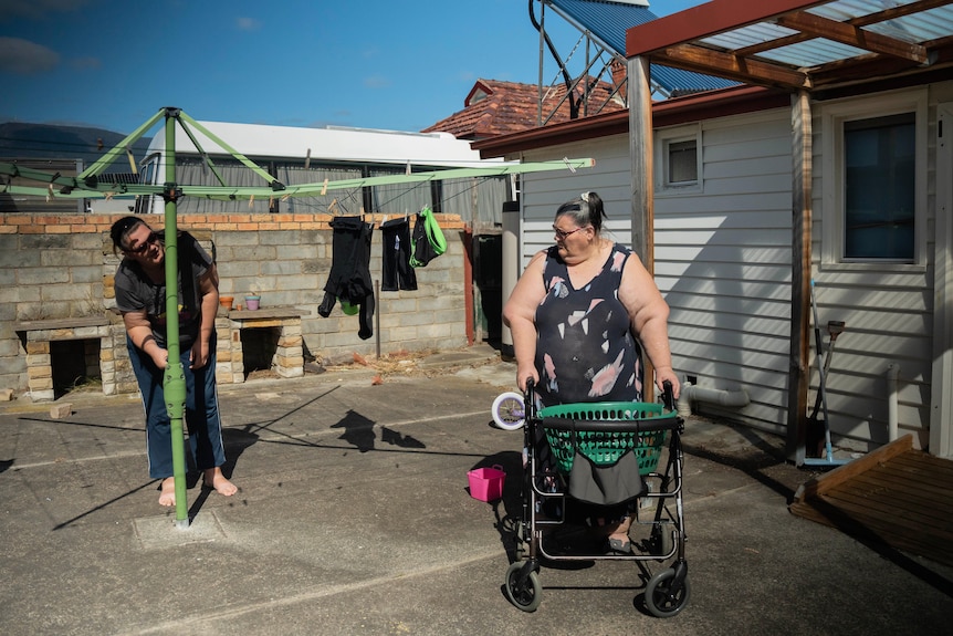 Young woman helps older woman get clothes off the clothes line in a cement back yard 