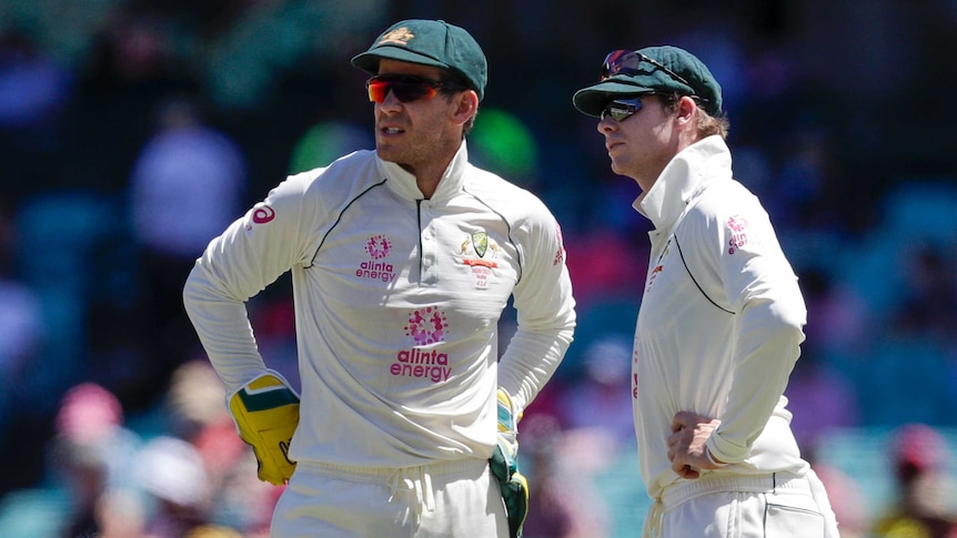 Tim Paine and Steve Smith stand looking off to one side, both standing with their hands on their hips