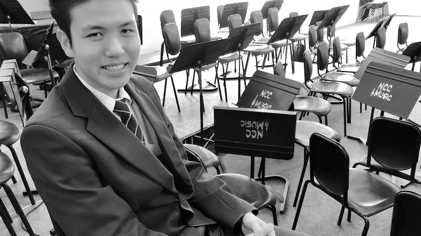 Black and white photo of a Chinese teenage school student sitting in a music room, smiling and looking at the camera.