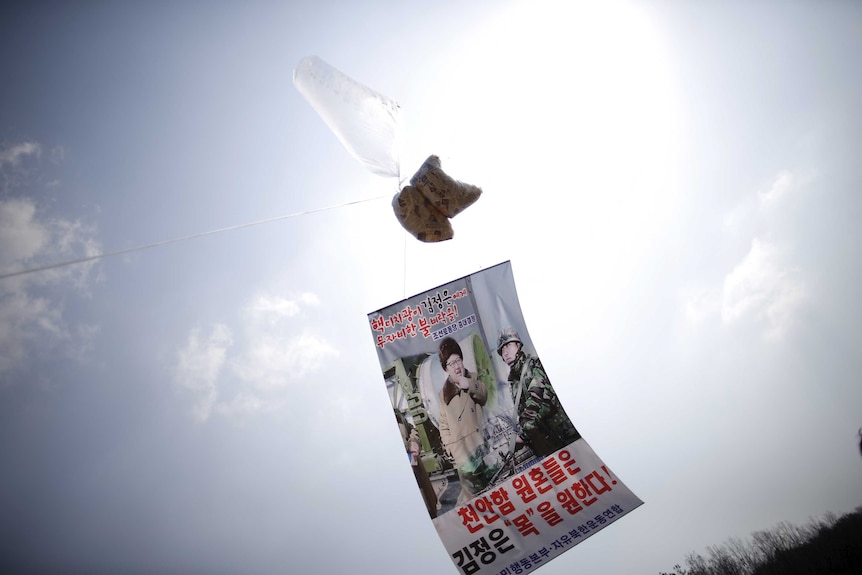 A transparent plastic long balloon flies in the air with a leaflet affixed to it.