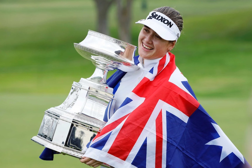 A golfer wrapped in an Australian flag holds the trophy after winning her first major title.