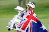 A golfer wrapped in an Australian flag holds the trophy after winning her first major title.