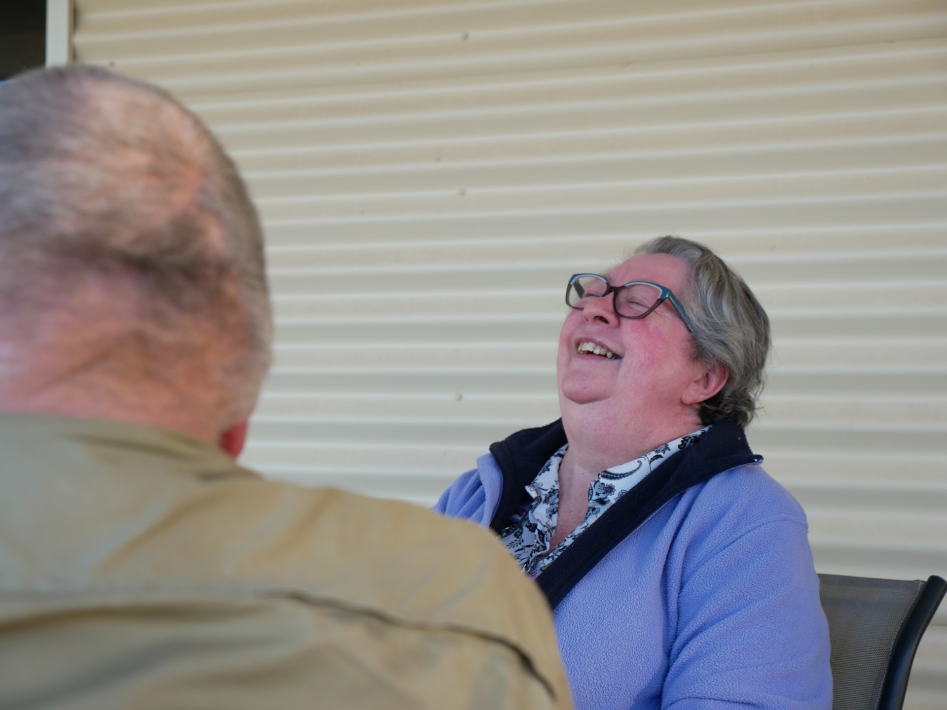 A woman with short hair and glasses throws her head back laughing.