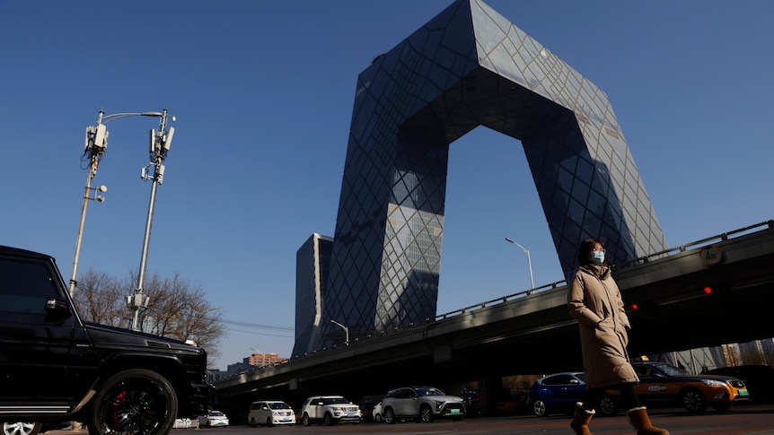 A woman walks past a unique tall building. 