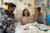 A photo of a woman laughing in a hospital bed with her son and daughter next to her