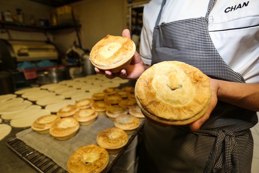 Chan Khun holding two pies with a tray of pies in the background.