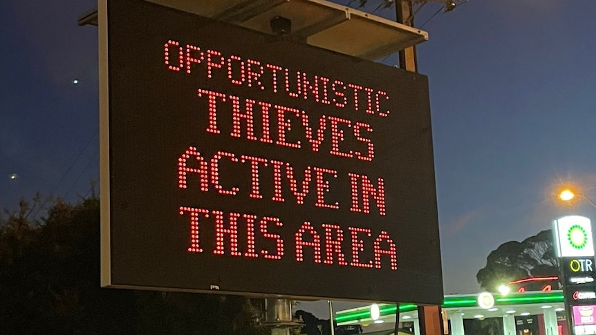 LED sign saying Thieves Active In This Area with petrol station in background taken at night time