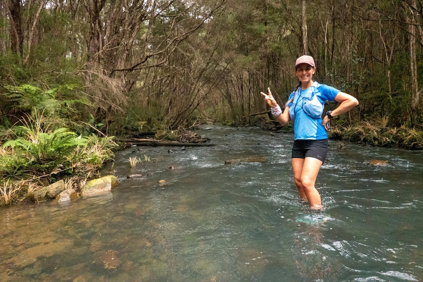 A woman calf deep in the middle of a flowing river surrounded by bushland.