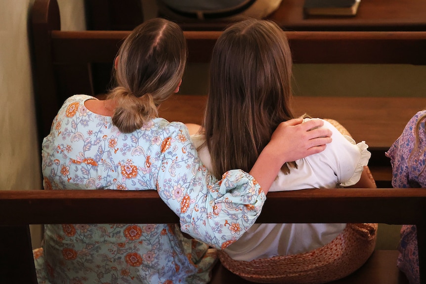 Two females embrace pictured from behind while sitting in church