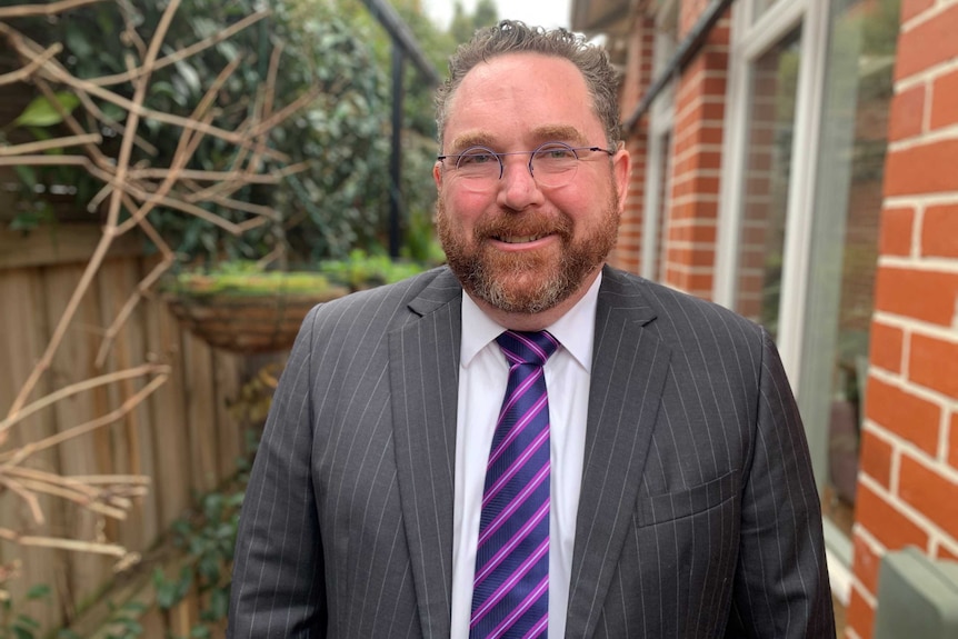 KPMG Australia's chief economist Brendan Rynne in a pinstripe suit standing outside a brick home.