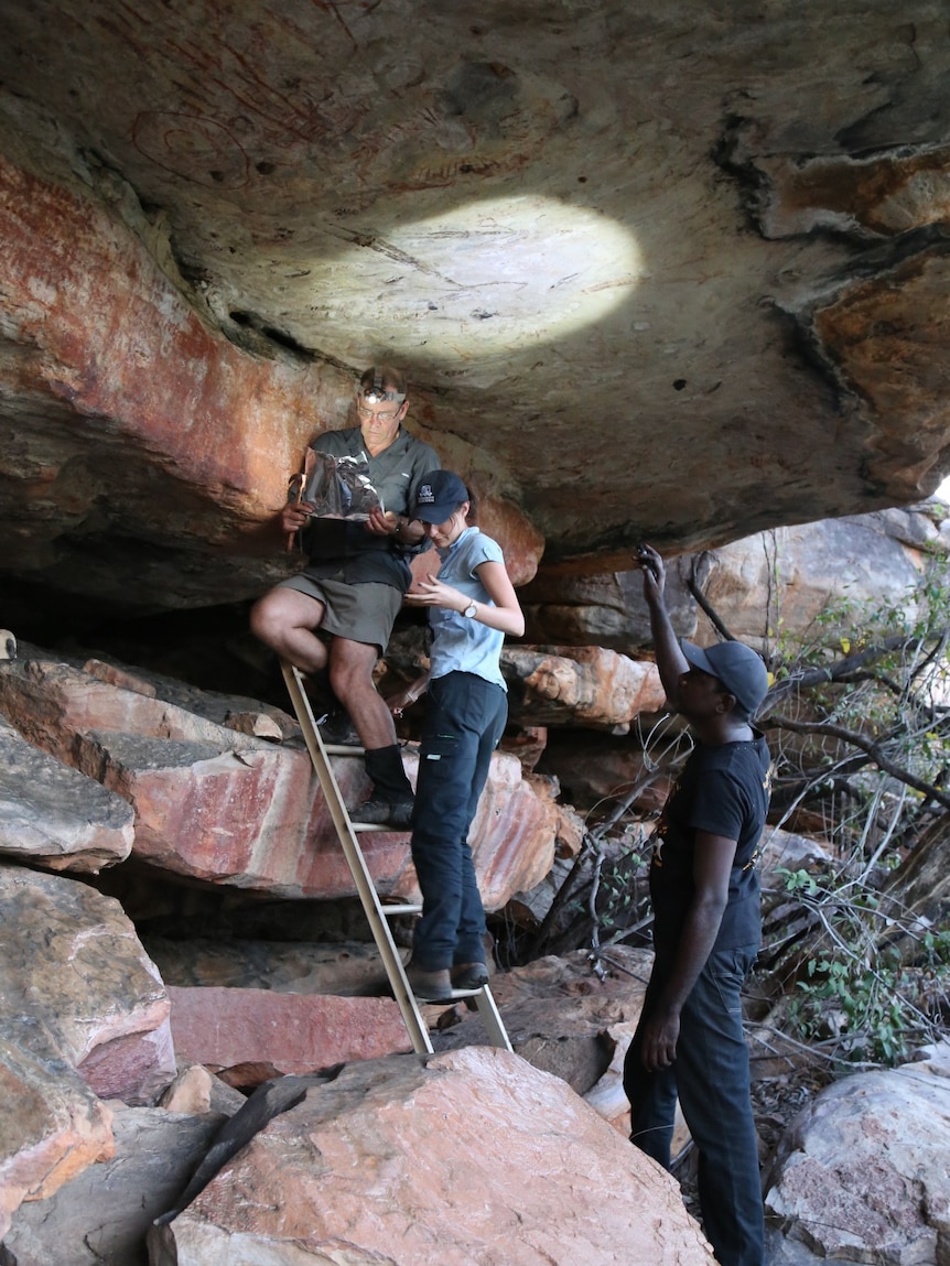 Two men and a woman standing under a rock overhang.