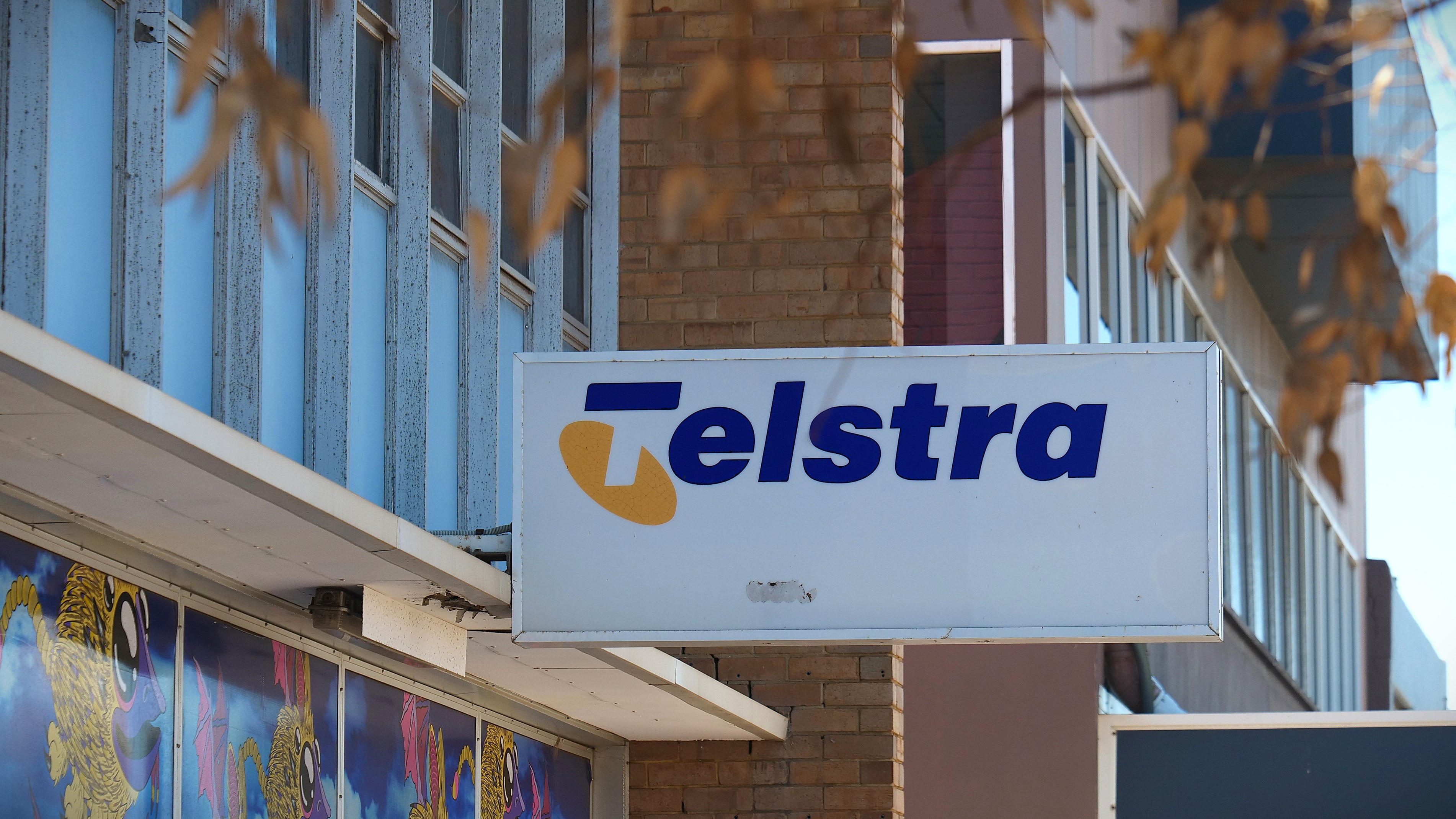 Primer plano de un cartel de Telstra frente a un edificio colorido. 