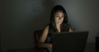 A woman sits in a dark room in front of a computer.