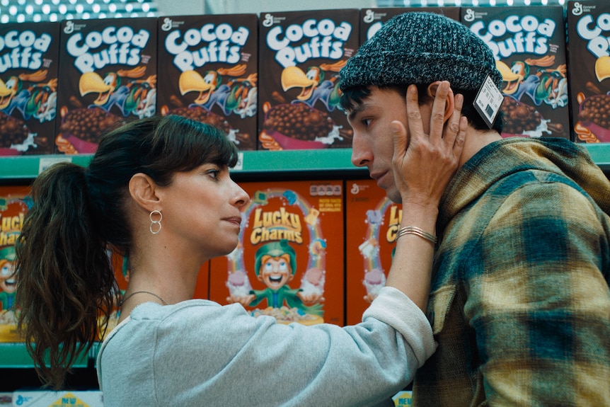 Maribel Verdú, a white Spanish woman with dark hair, and Ezra Miller, a white male-presenting person, embrace in a supermarket.