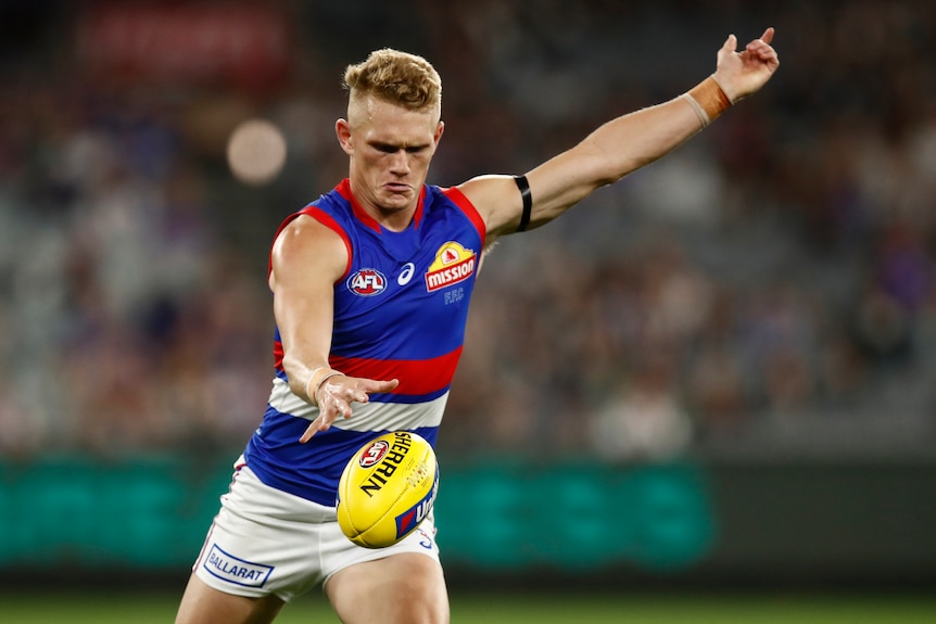 A Western Bulldogs AFL player drops the ball with his right hand as he prepares to kick.