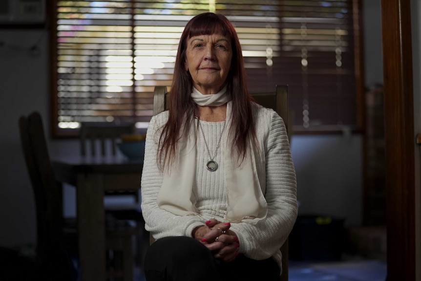 An older lady sits in front of vertical blinds.